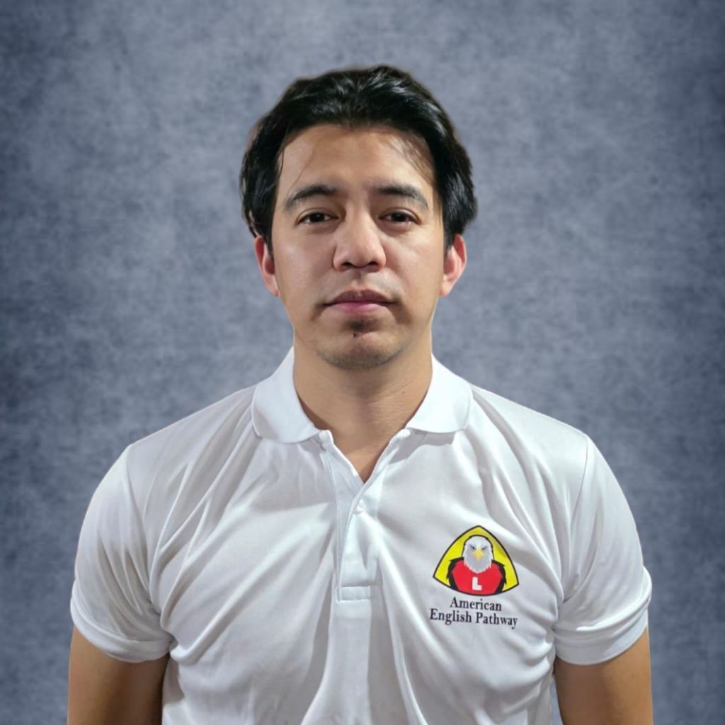 Man in a white polo shirt with American English Pathway logo, standing against a gray background.